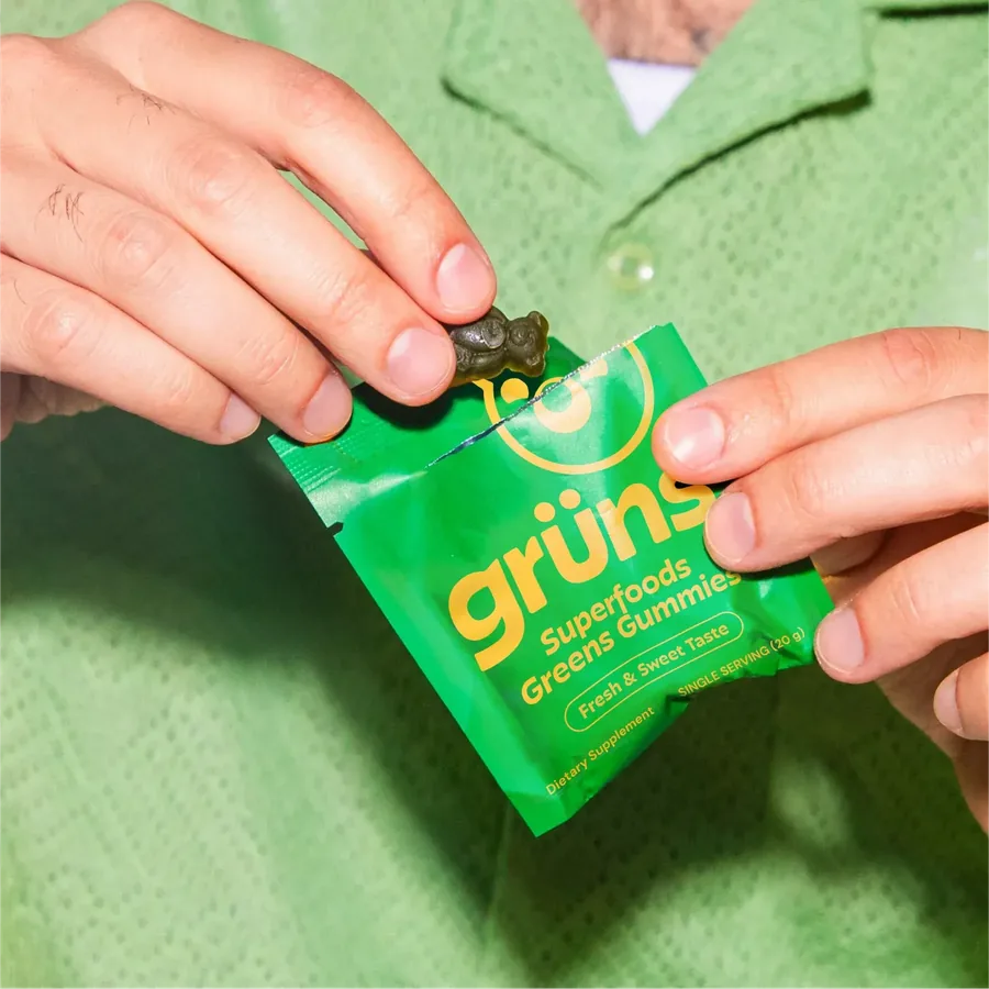 A single Grüns daily sachet held in one hand, ready to open