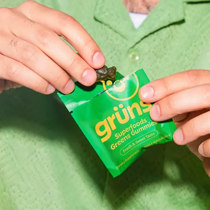 A single Grüns daily gummy pack held in one hand, the unit the per-day price is based on